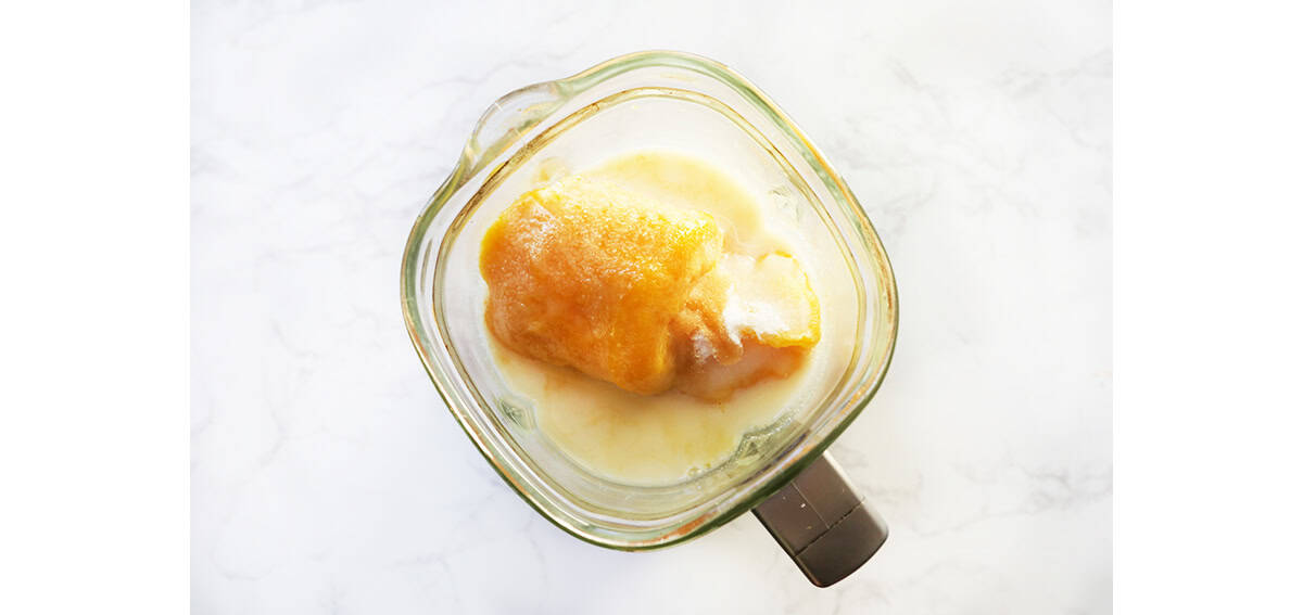 Top view of blender with orange juice concentrate and milk inside.