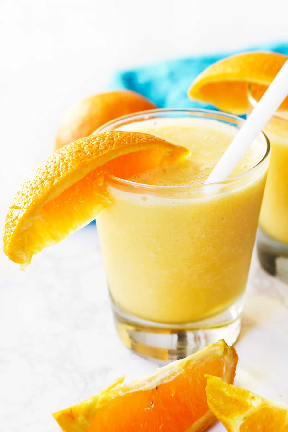 An orange julius drink with a straw inside and an orange slice on the rim.