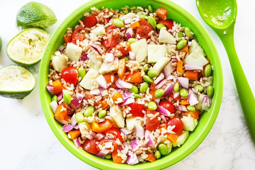 Vegetable rice salad in a bowl with a serving spoon next to a squeezed limes. 