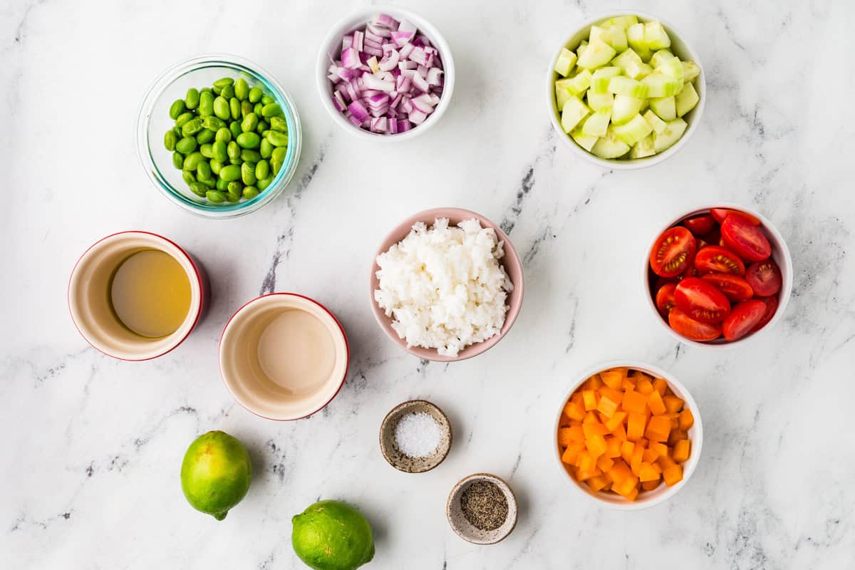 Ingredients for veggie rice salad in individual bowls, lined up on a white counter.
