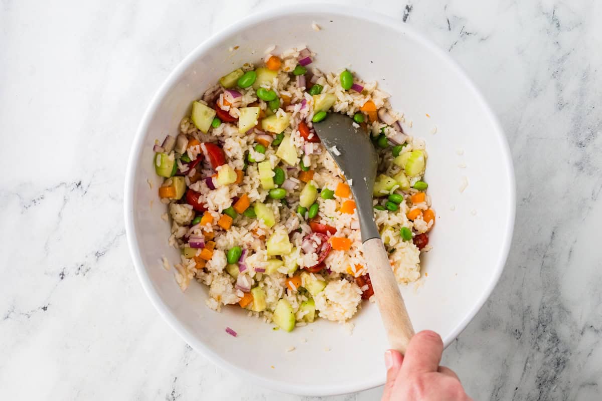 Hand stirring the salad in the mixing bowl.