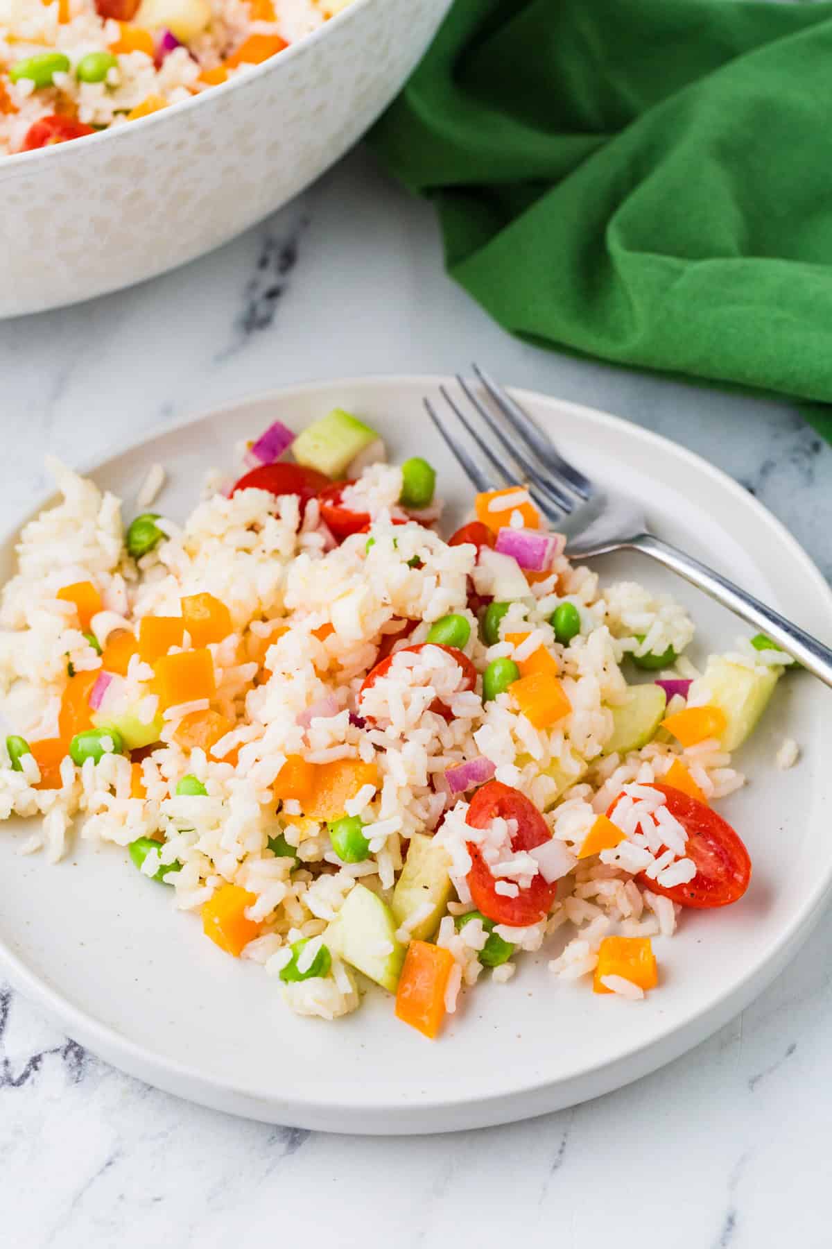 Plate with a serving of vegetable rice summer salad and a fork, next to bowl filled with the salad.