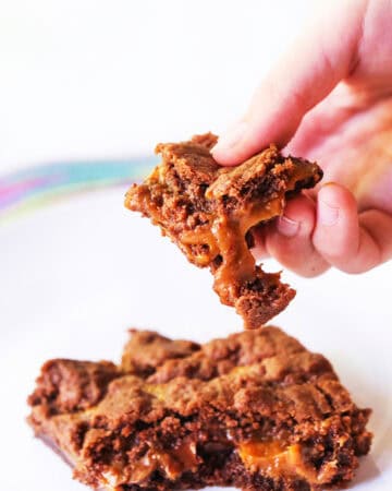 Close-up of caramel brownies with a hand holding a piece.