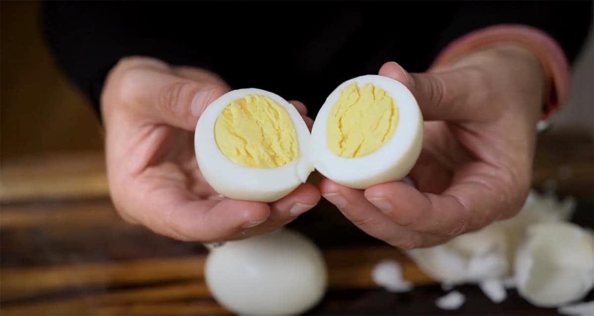 Hands revealing the perfectly cooked center of a hard-boiled egg.