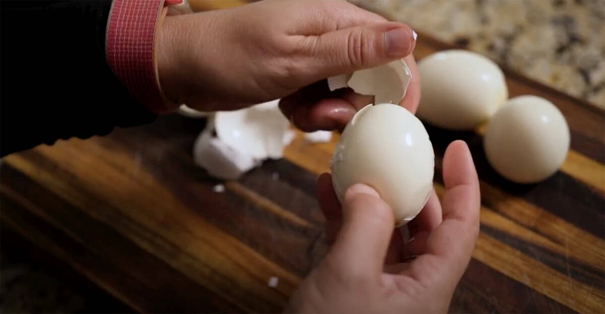 Hands peeling a hard boiled egg.
