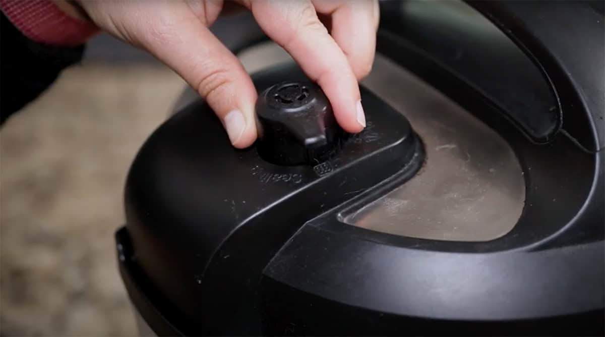 Fingers moving steam release valve on an Instant Pot to sealing.