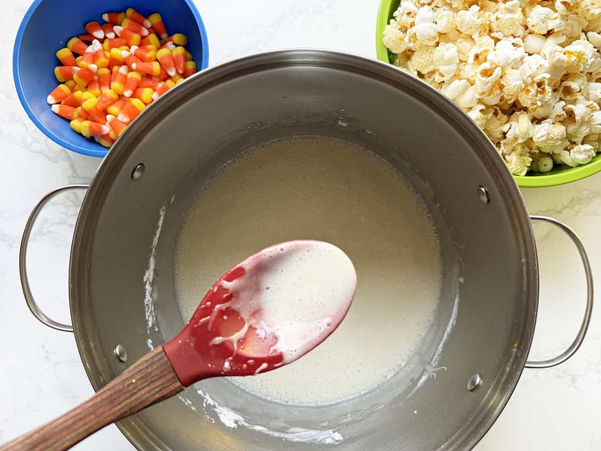 Marshmallow mixture in pot, next to popcorn and candy corn.