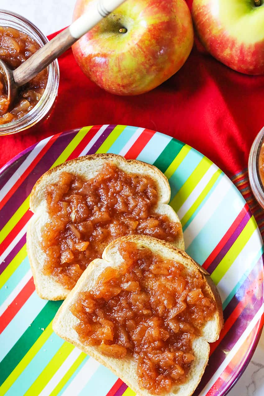 Two pieces of toast slathered with apple butter, next to two apples.