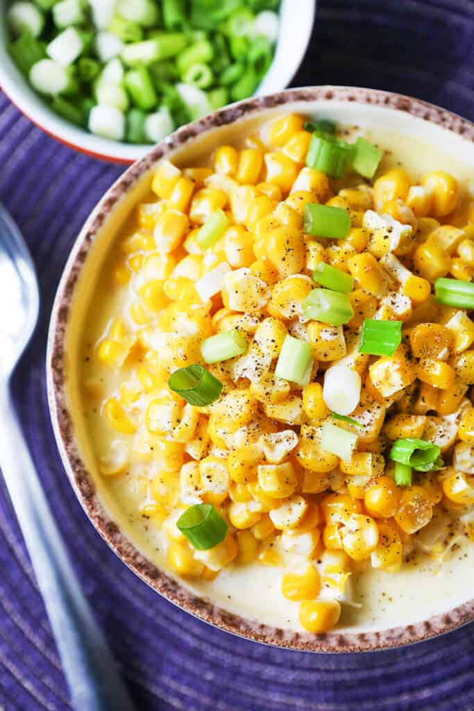 large bowl of creamed corn topped with green onions with a serving spoon next to it