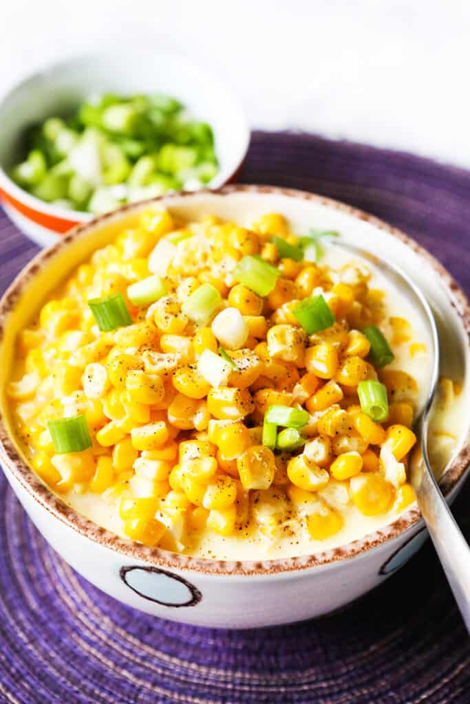 spoon stuck into a bowl of crock pot creamed corn with green onions on top