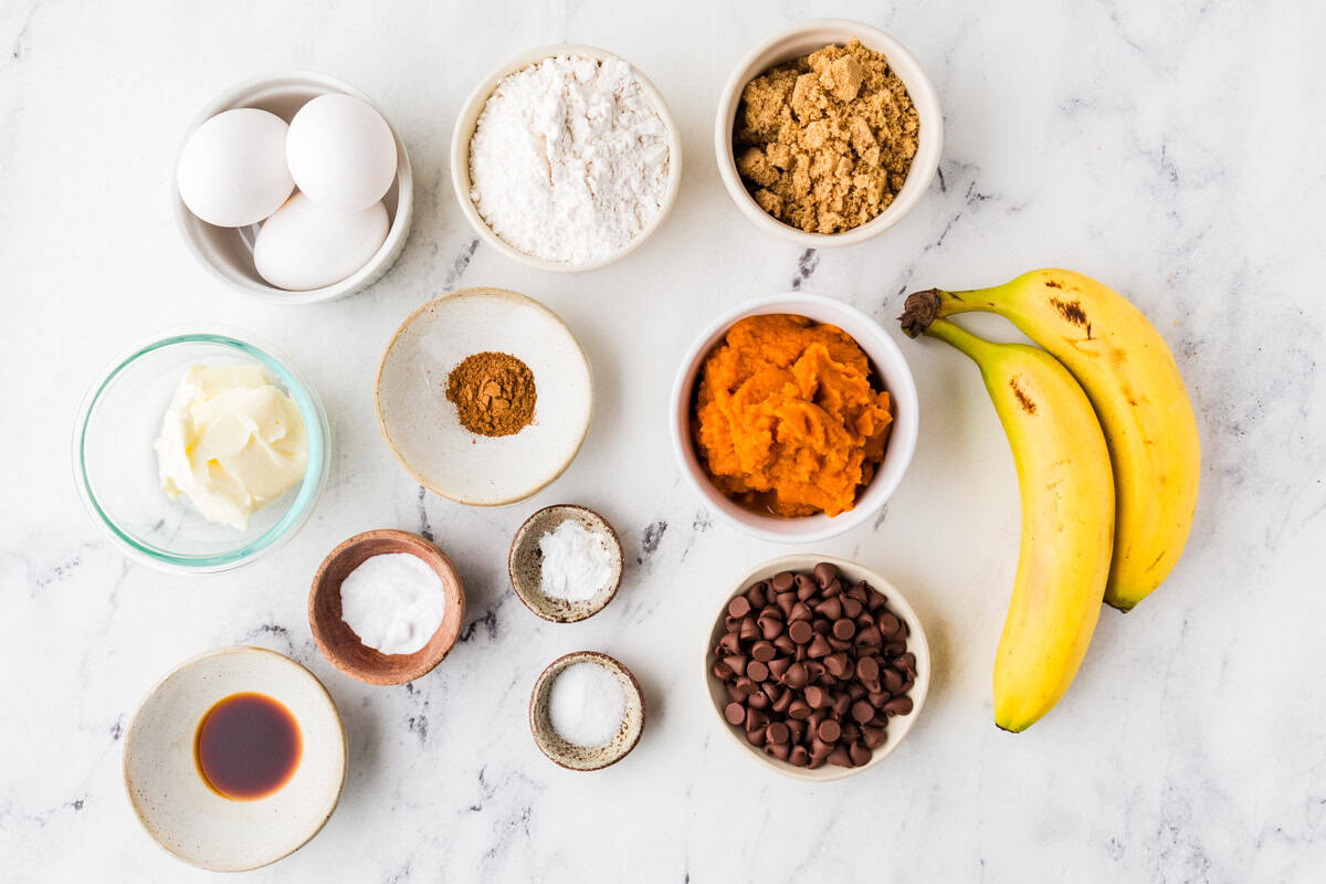 Ingredients for pumpkin banana bread lined up on a white marble countertop.