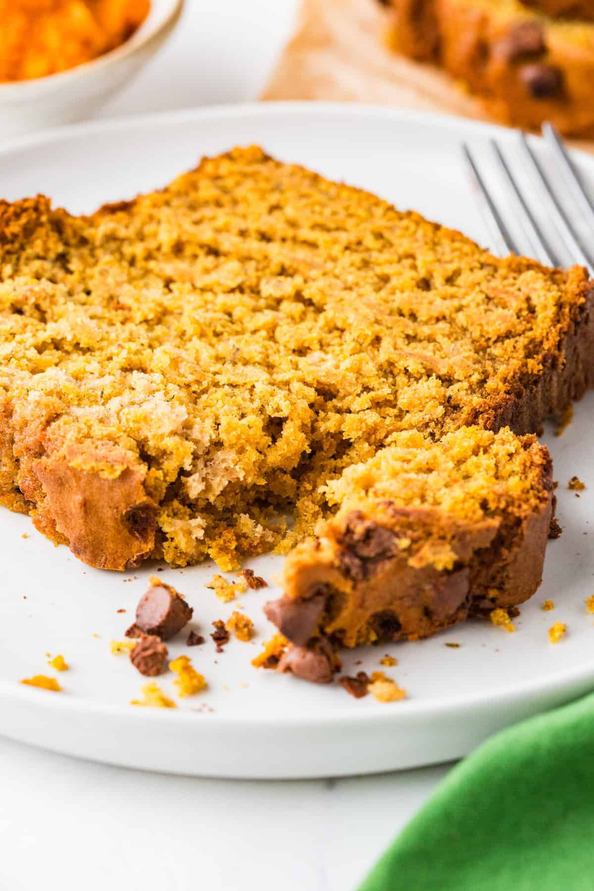 Slice of pumpkin bread on a plate with a bite separated and a fork nearby.