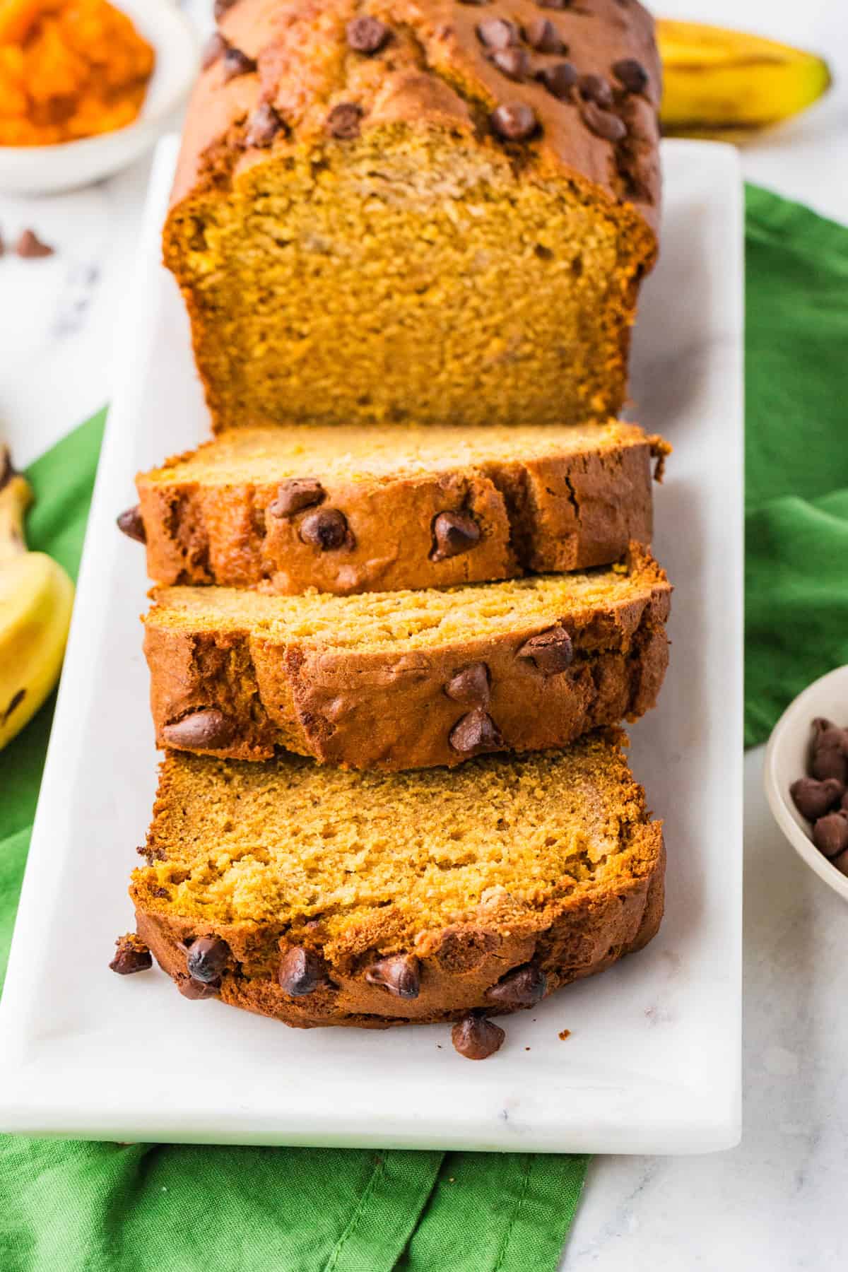 Loaf of pumpkin banana bread with slices cut off on a serving tray.