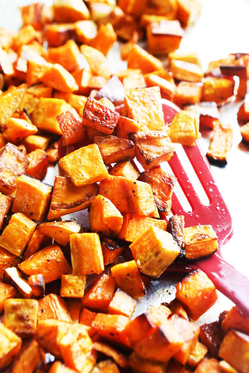 Spatula in a batch of roasted sweet potatoes on a baking sheet. 