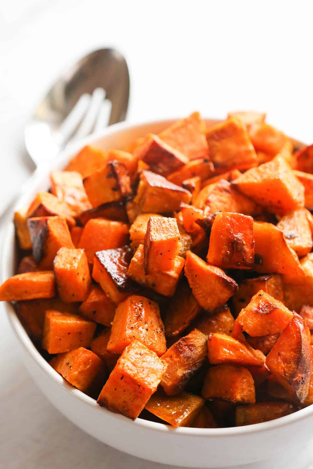 Close up of a bowl of roasted sweet potatoes with a serving spoon nearby.