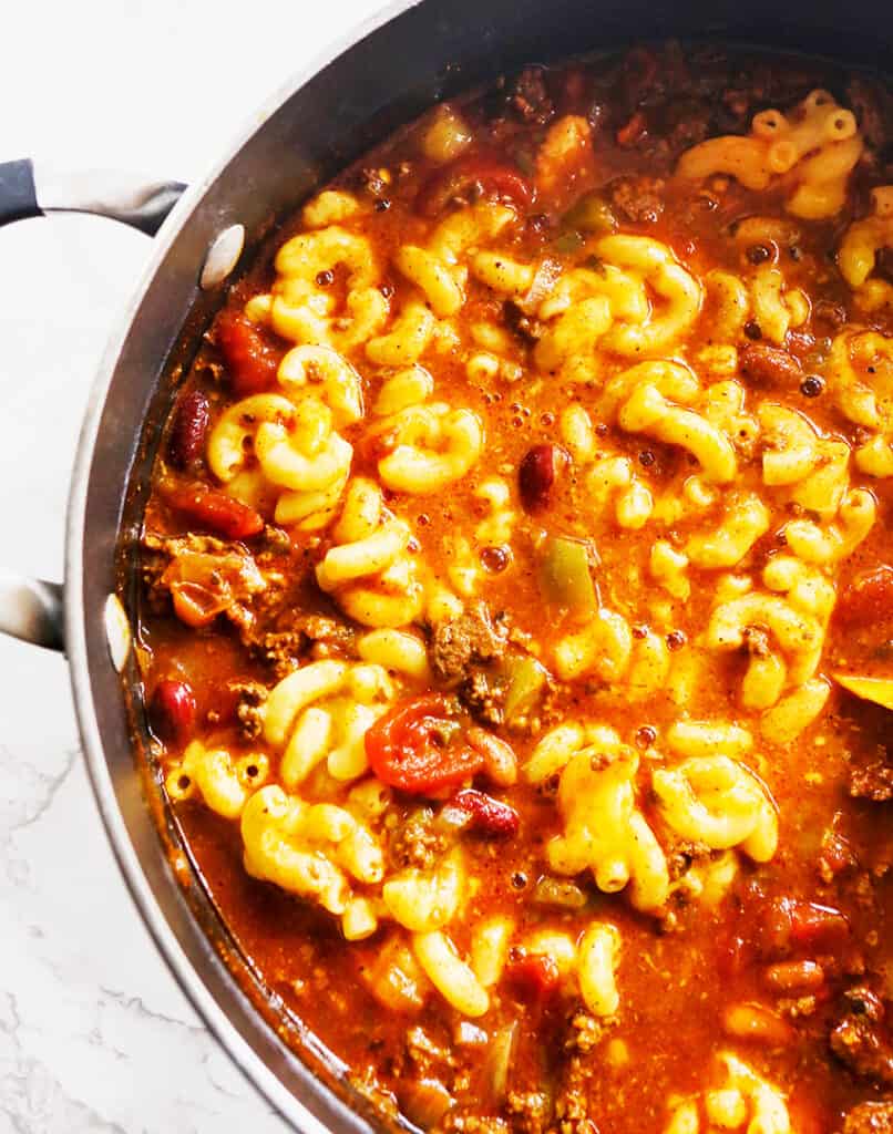 Half of a view of a skillet with chili mac inside with chunks of tomatoes in the sauce, ready to serve. 