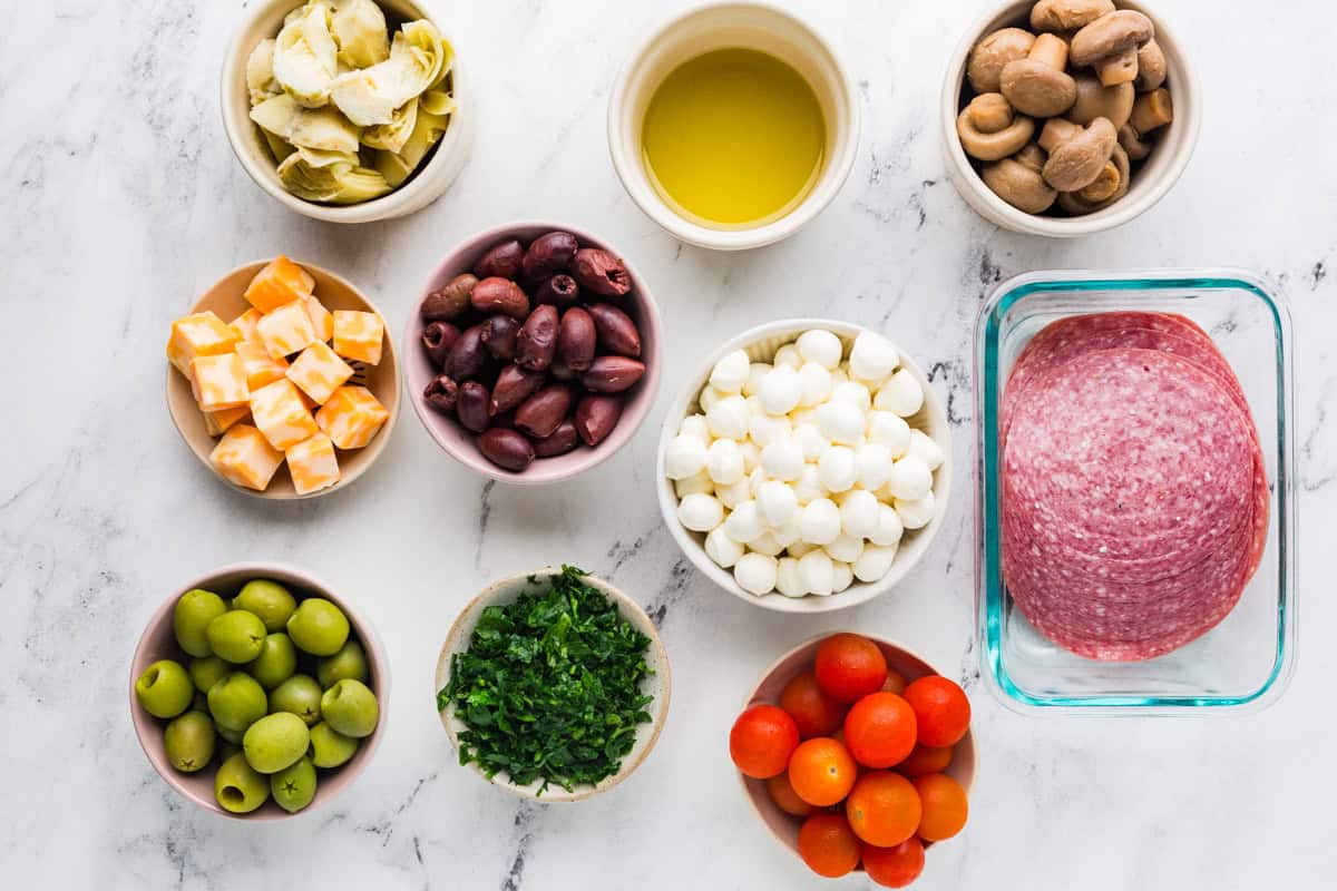 Ingredients for antipasto skewers in individual bowls on a white counter.