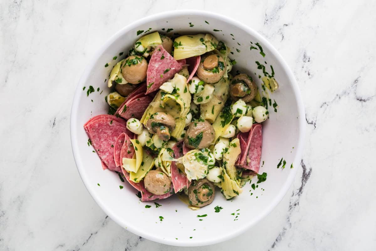 Meat, mushrooms, artichokes and cheese balls in a marinated mixture in a bowl.