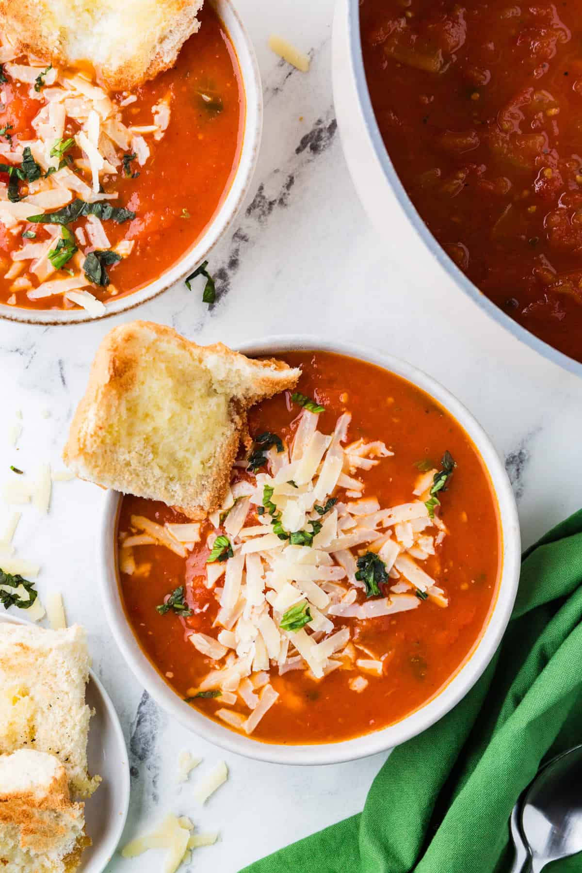 Top view of two bowls of tomato soup topped with cheese side by side.