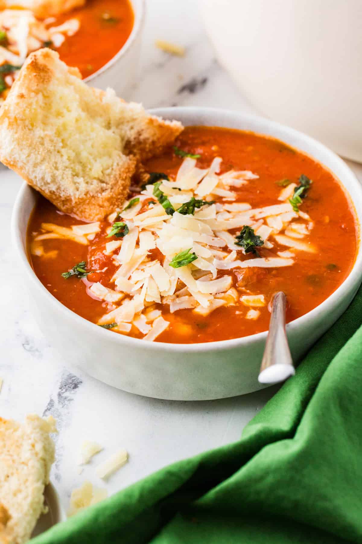 Bowl of roasted tomato soup, topped with a crusty piece of buttered bread and parmesan cheese.