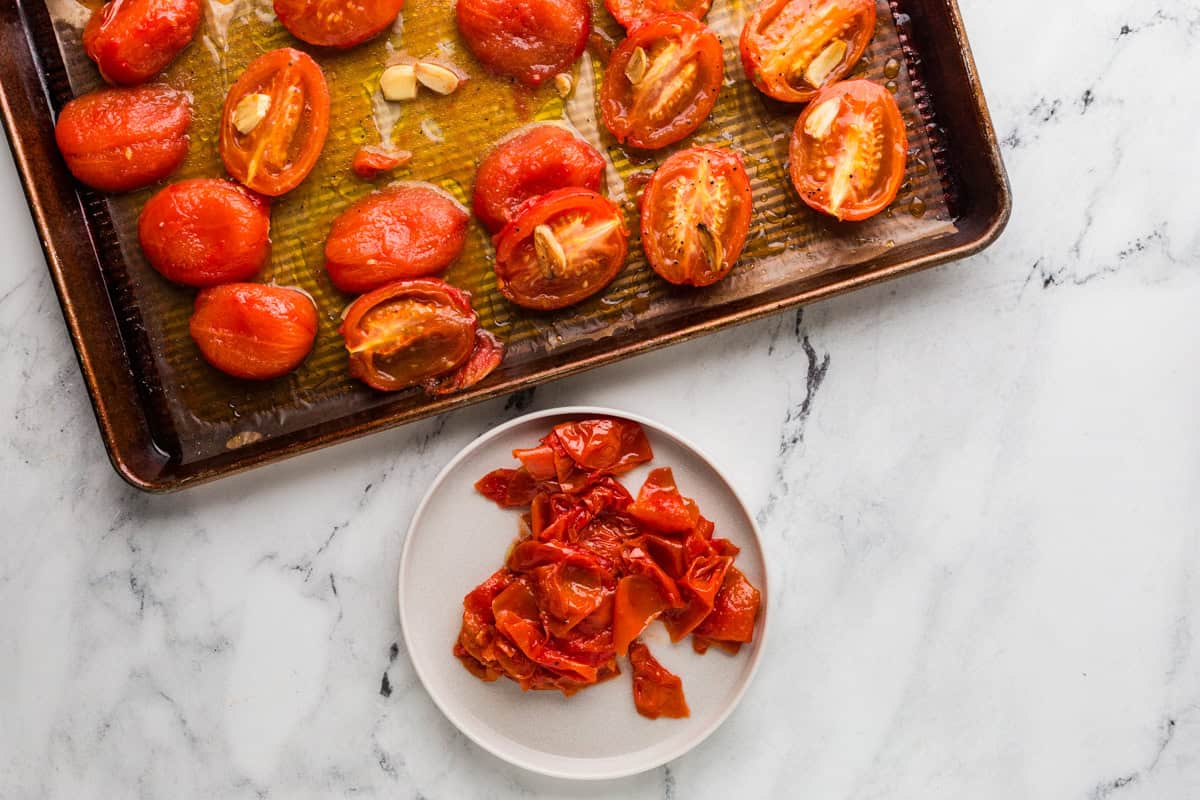 Roasted tomatoes on a baking sheet with garlic.