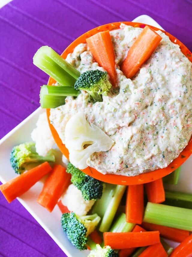 Creamy vegetable dip in a bowl on a platter with cut up veggies for dipping. 