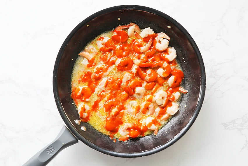 buffalo sauce drizzled over shrimp in a skillet