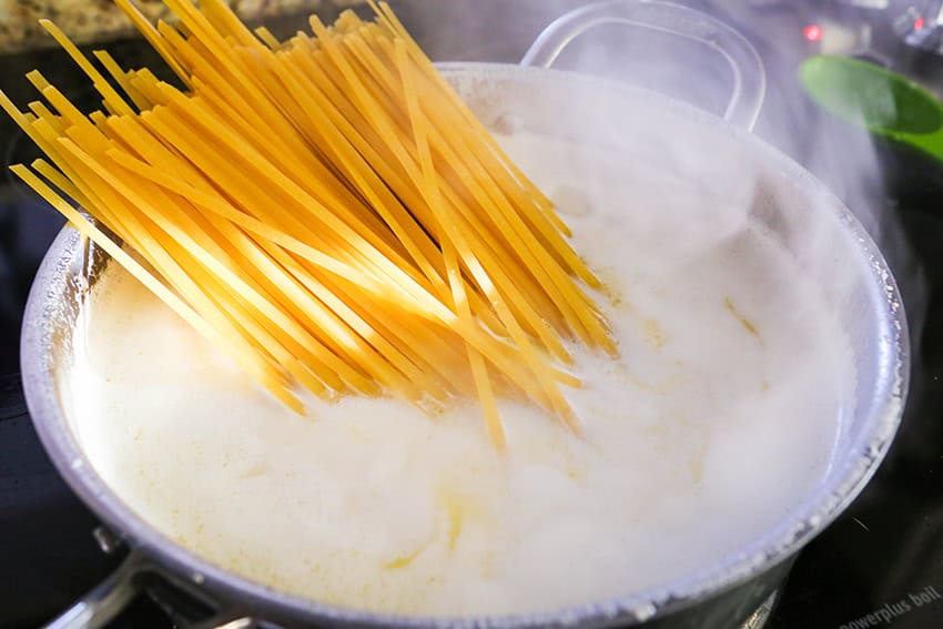 Cooking spaghetti in boiling water with steam rising, close-up view.