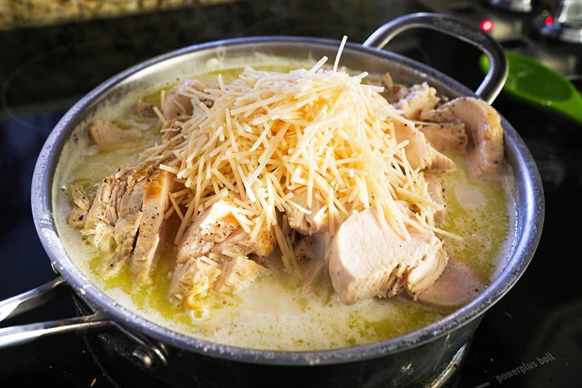 Hearty chicken and cheese soup with shredded cheese on top in a large pot.
