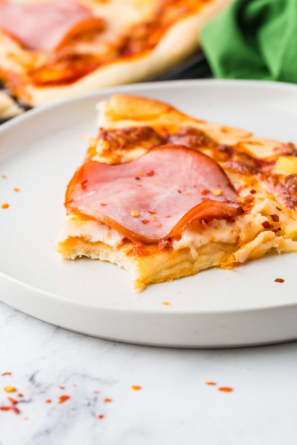 Slice of pizza with a bite taken out, on a plate.