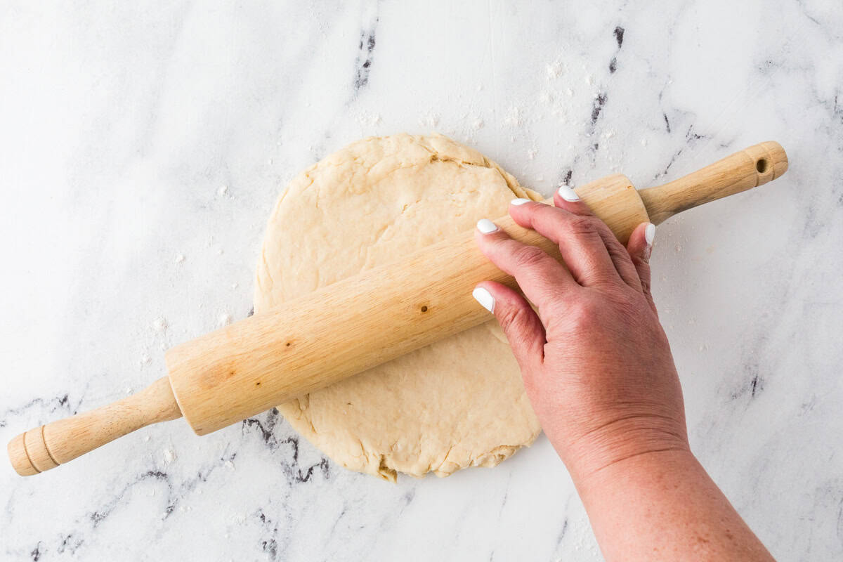 Hand rolling out pizza dough with a rolling pin.