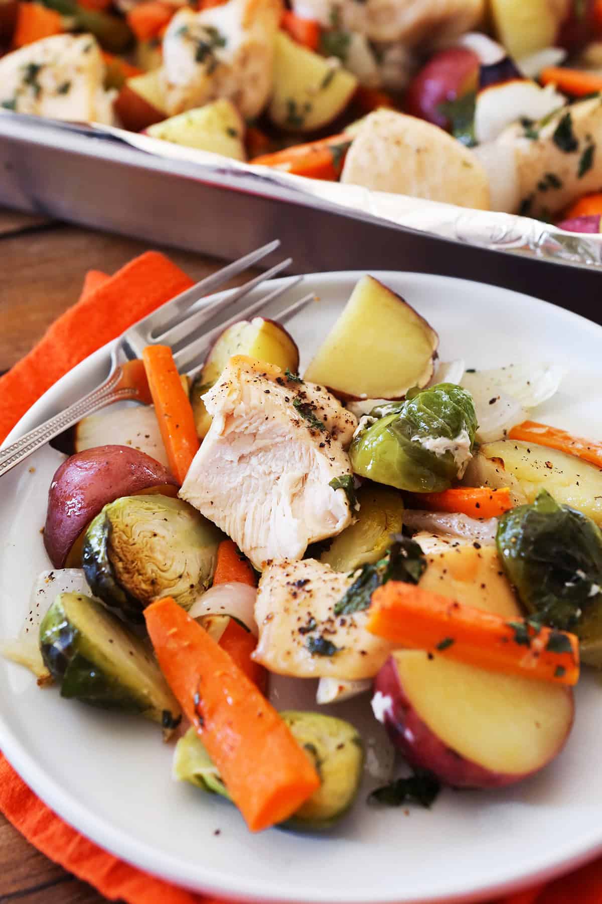 Plate of cooked chicken and veggies sitting next to a pan.