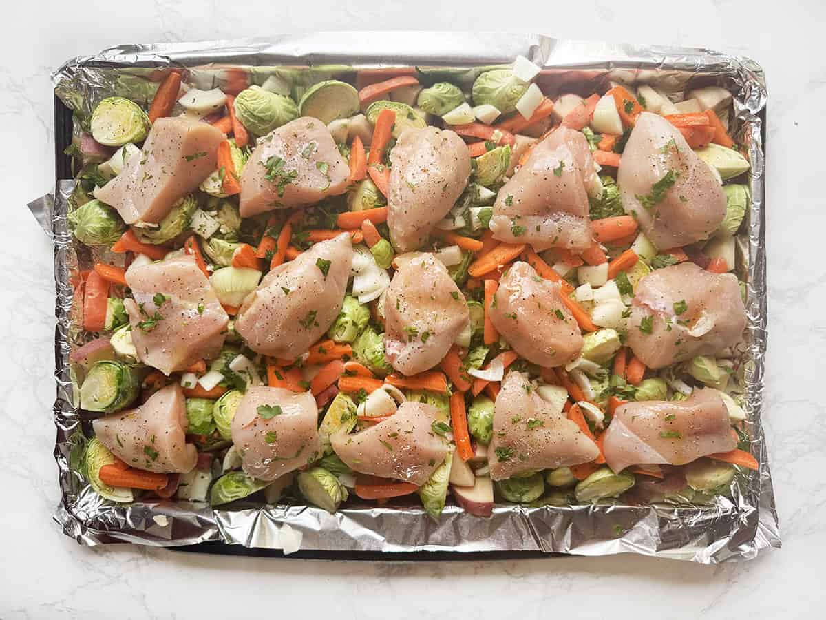 Pan of chopped vegetables with chicken pieces on top, before baking.