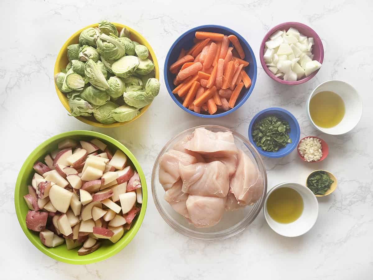 Ingredients for herb roasted chicken and veggies in individual bowls, lined up on a counter.