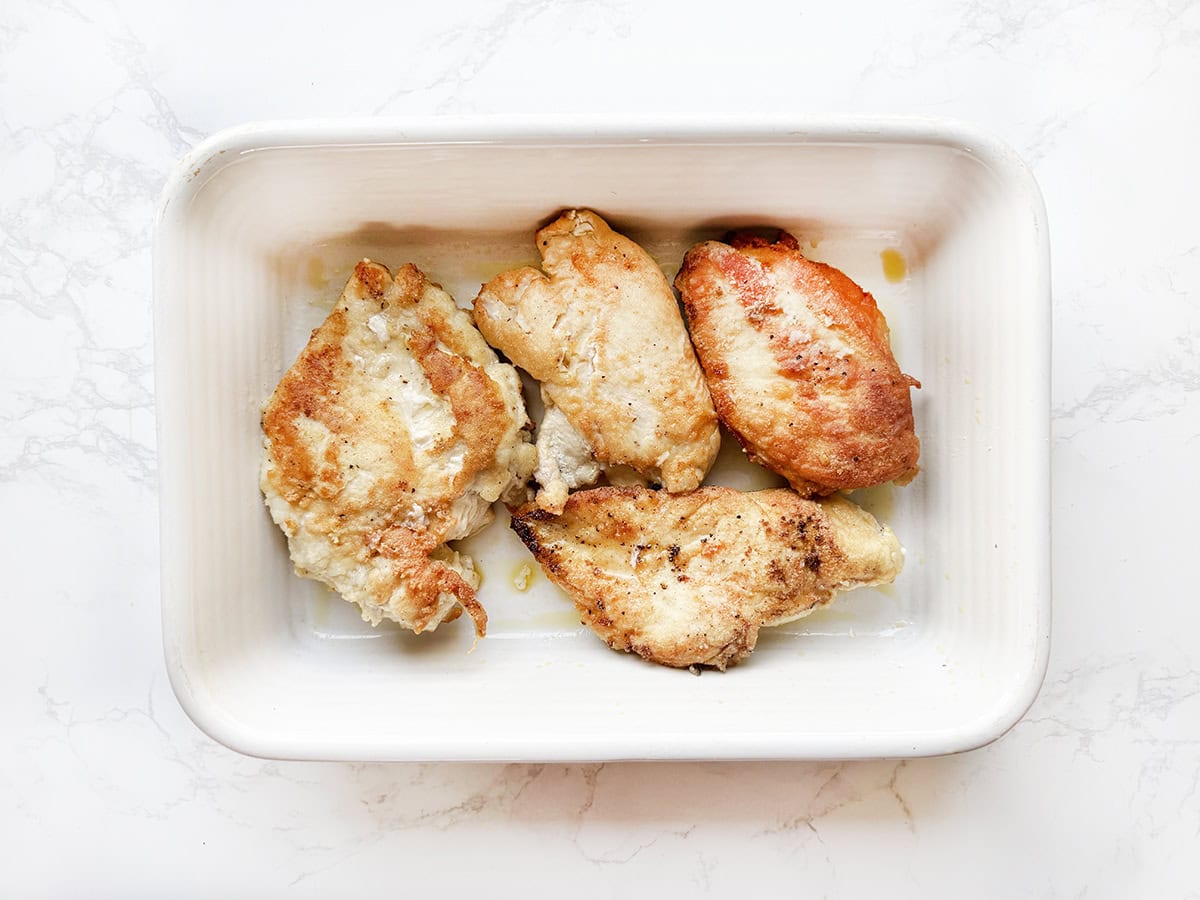 Four pieces of chicken after being pan fried, lined up in a baking dish.
