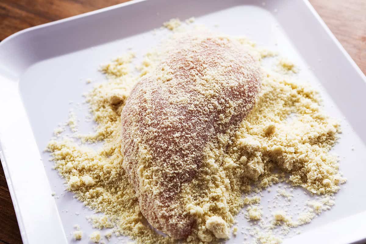 A chicken breast on a plate, coated in a flour mixture.