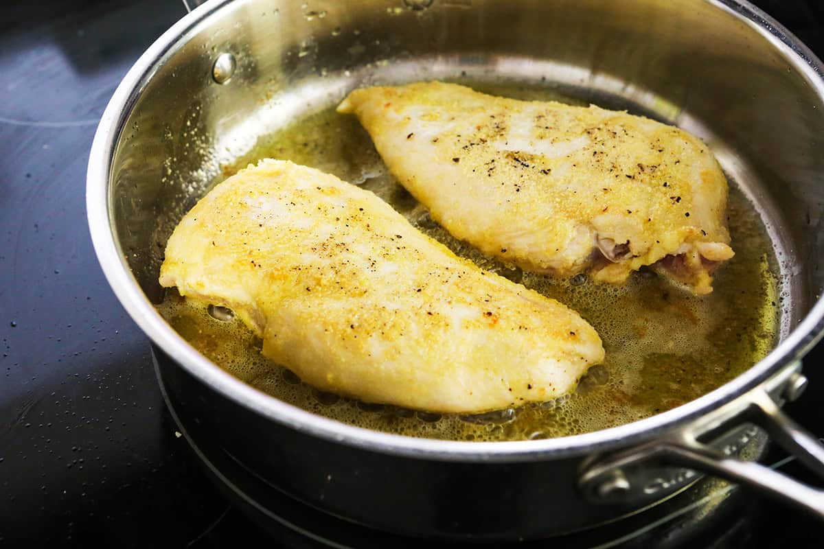 Two chicken breasts being fried in a pan of oil.