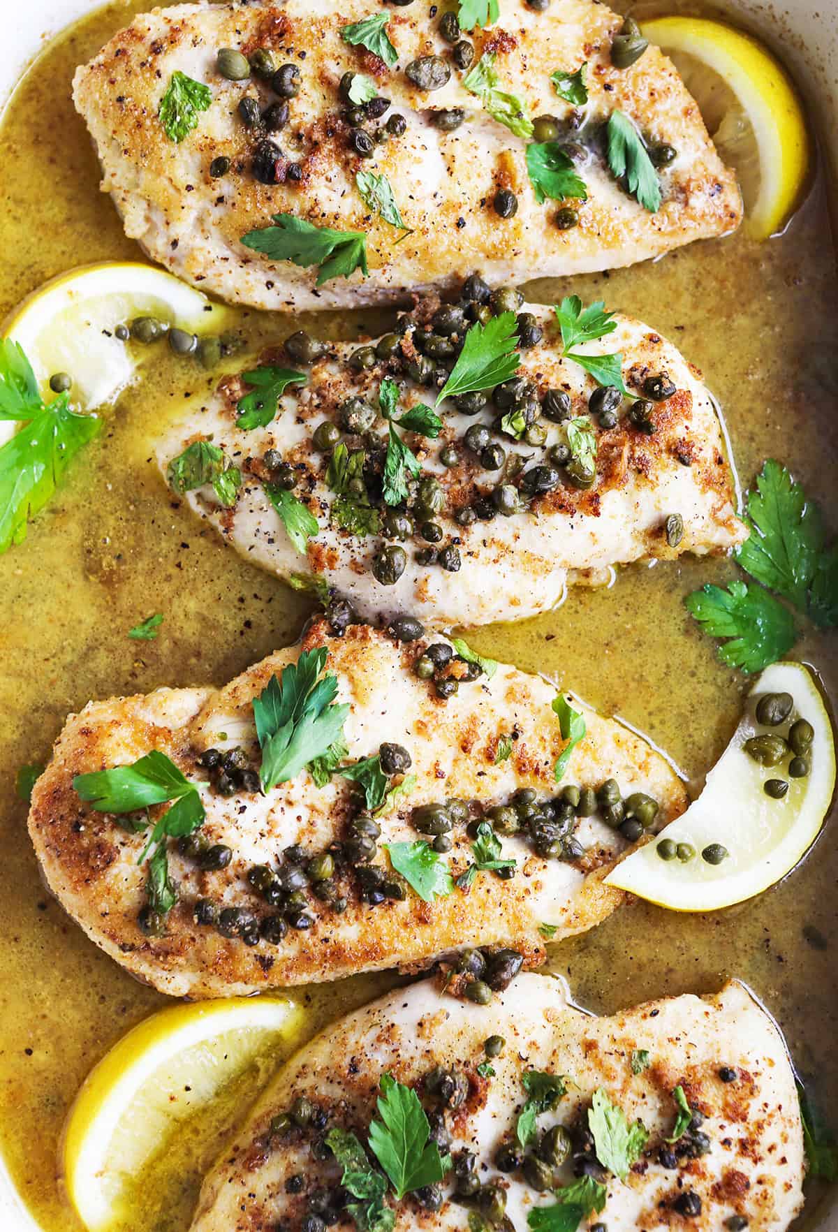 Top view of chicken piccata in a sauce mixture inside a baking dish.