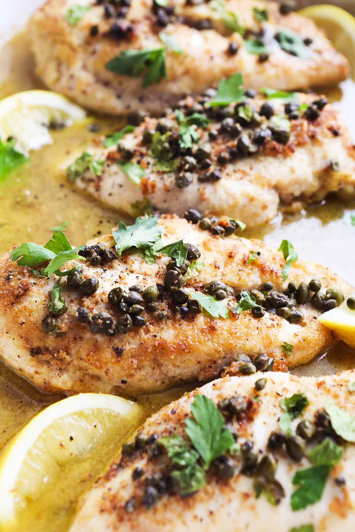 Four cooked pieces of chicken piccata, swimming in a lemon sauce in a pan.