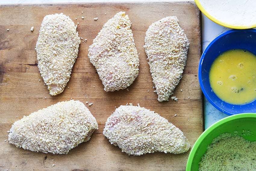 chicken breasts on a cutting board coated with breadcrumbs