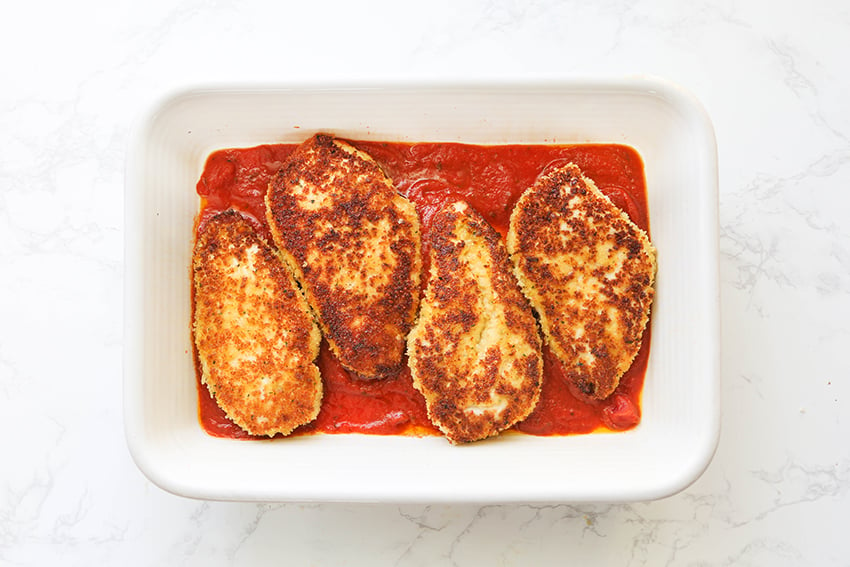 golden brown chicken breasts in a baking dish with marinara sauce