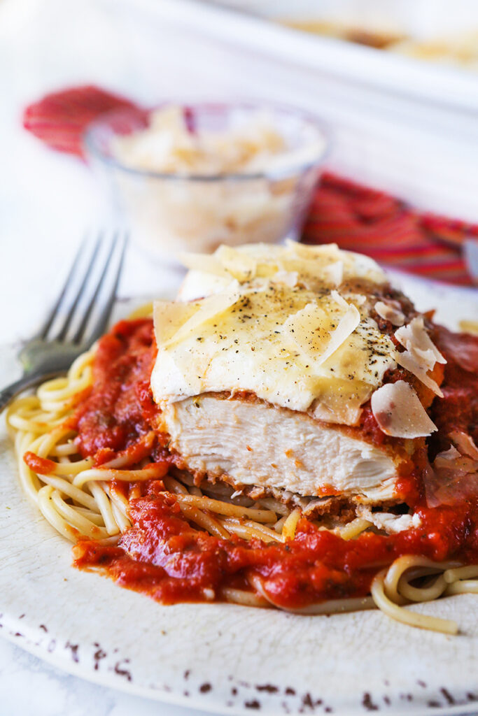 A bed of pasta and sauce with a chicken breast cut open and shaved parmesan on top.