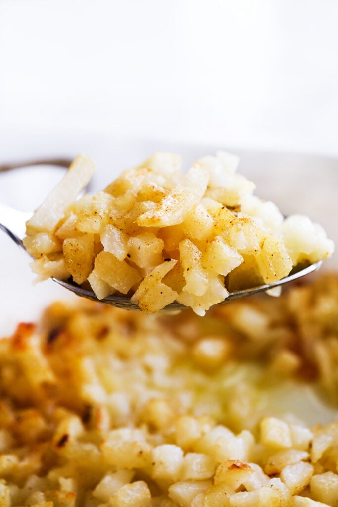 close up image of a spoon full of hashbrown casserole on top of the serving platter