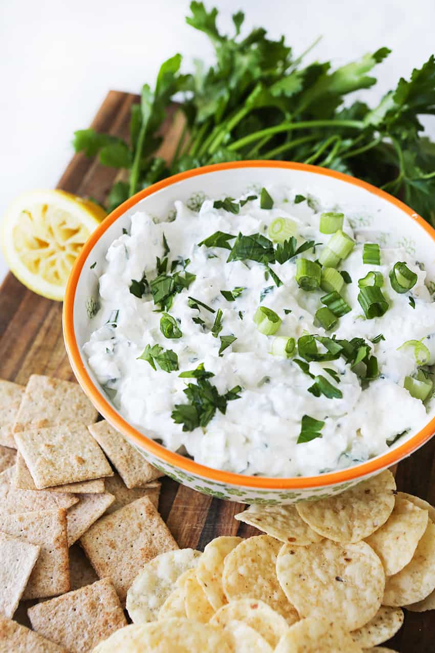 Feta cheese dip in a bowl with sliced green onions over the top and chips and crackers around the bowl.