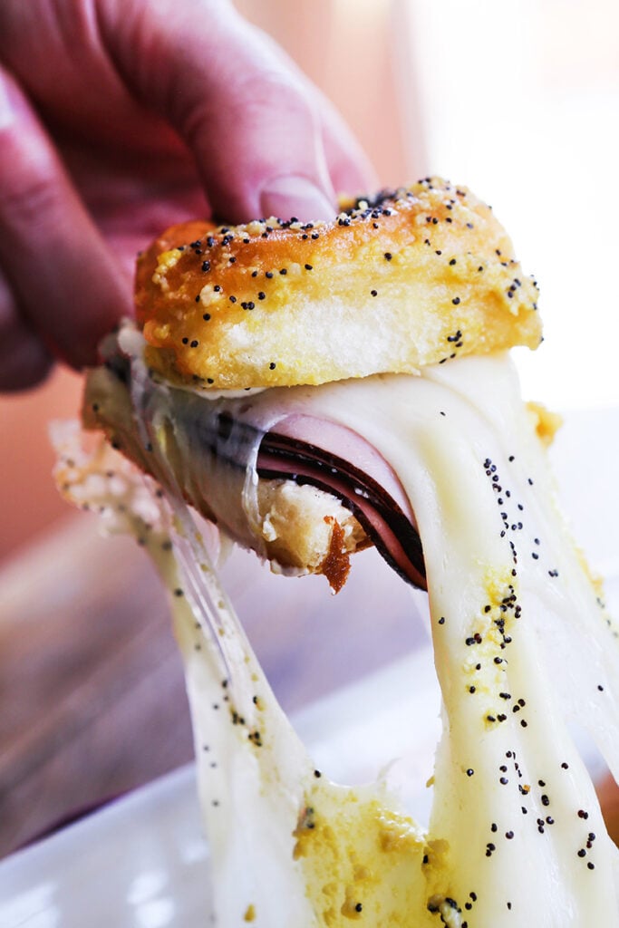 a hand pulling up a single ham and cheese slider from a pan of them 