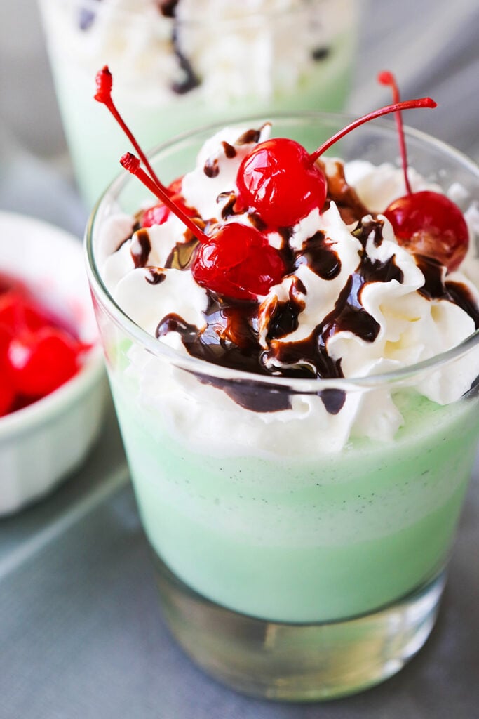 copycat shamrock shakes lined up next to each other with chocolate drizzled over top and cherries