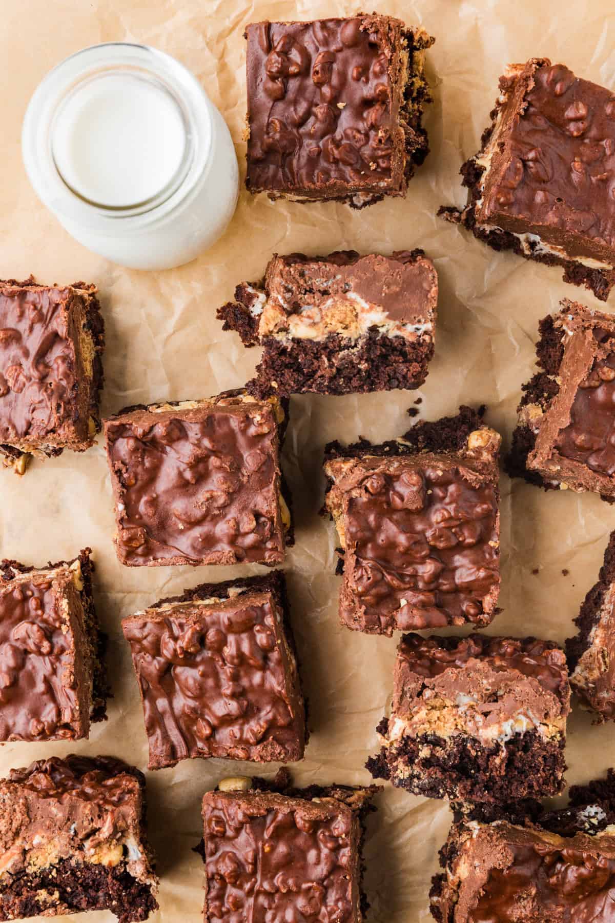 Top view of brownies cut and lined up on a sheet of parchment paper, with a glass of milk on the side.