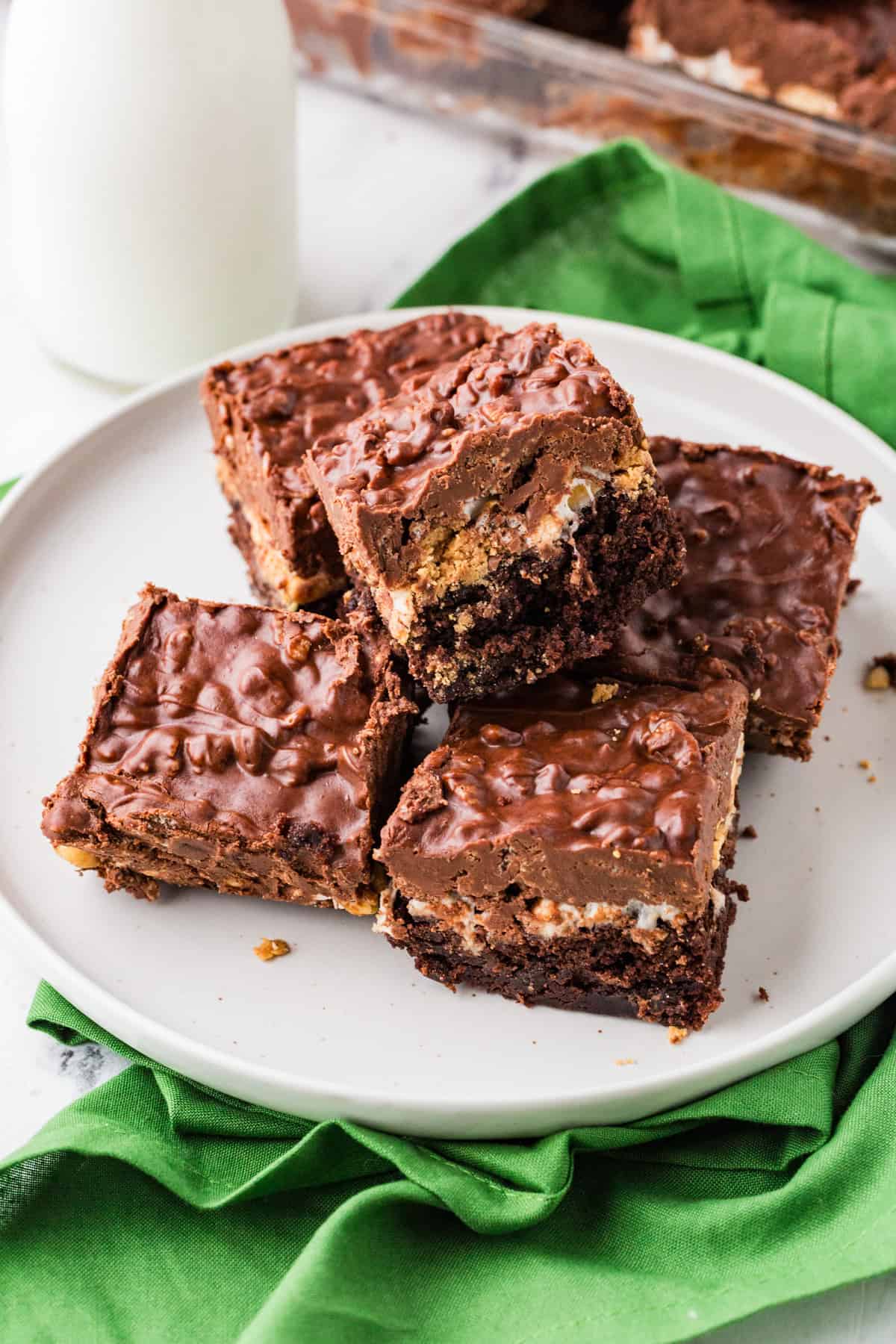 Plate stacked with decadent brownies containing multiple delicious layers, with a glass of milk nearby.