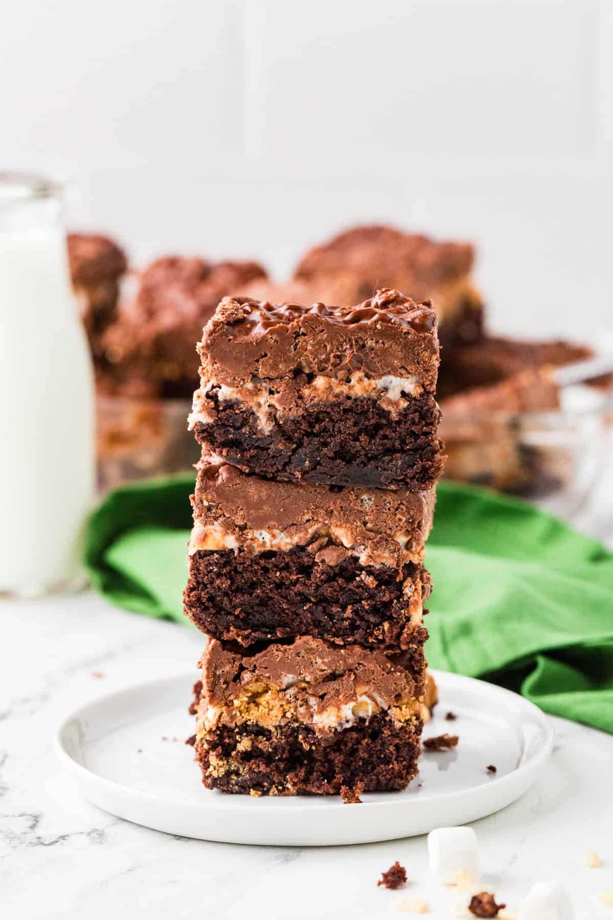 Three multi-layered brownies stacked on top of each other on a white plate.