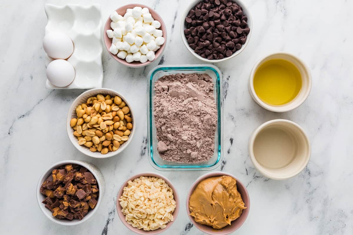 Ingredients for marshmallow brownies in individual bowls lined up on a white counter.